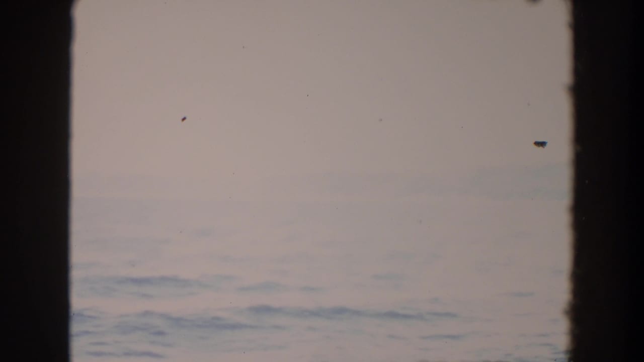 Pale ocean surface with haze and faint distant hills.