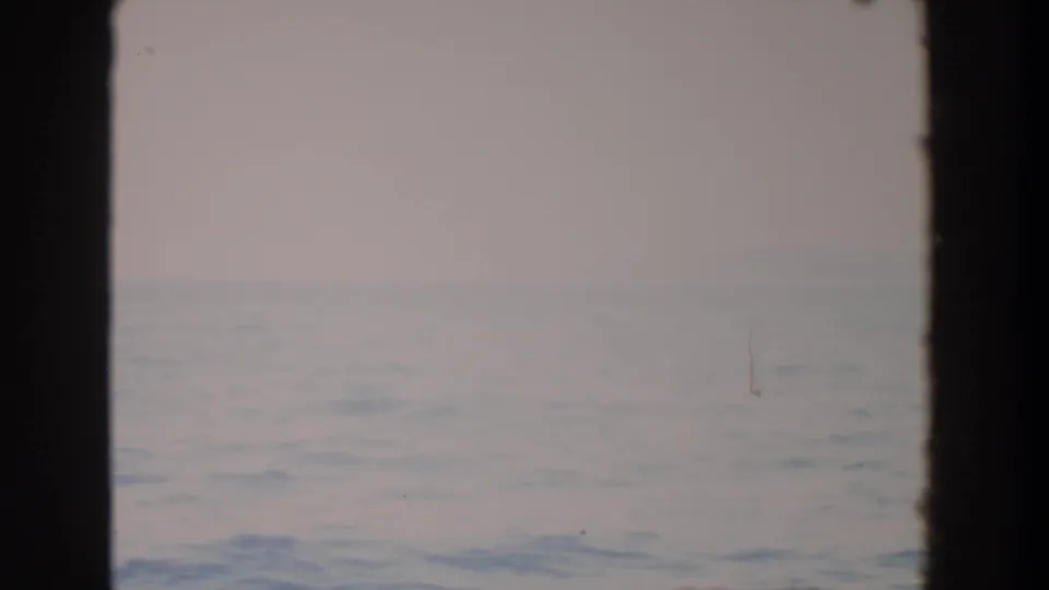 1964 Washington-associated 8mm frame showing a muted ocean horizon through dark window mullions, with soft sky and visible film grain.