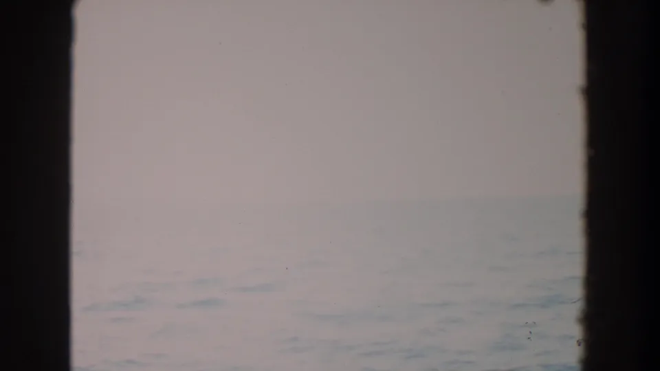 Muted blue-gray water fills the lower frame while a hazy horizon and dark window borders emphasize the passenger-window viewpoint.