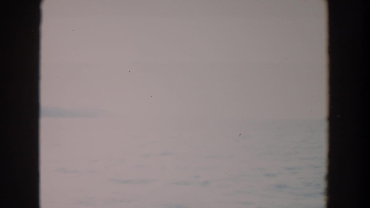 Soft, pale opening frame of water and overcast sky from 1964 Washington home-movie footage, bordered by dark film edges.