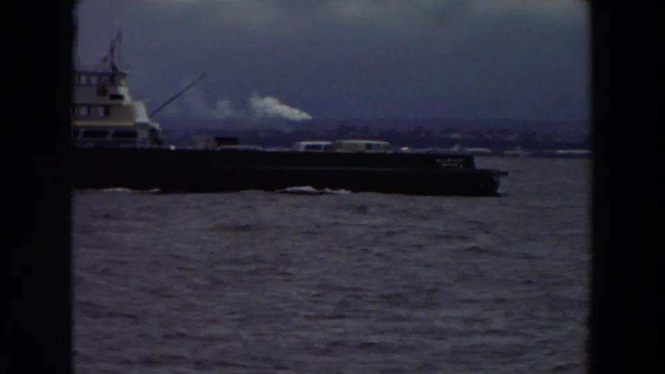 A large ferry-like vessel moves across a Washington river scene, with cloudy sky and distant shoreline behind it.