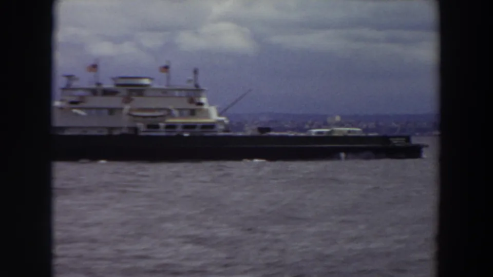 A ferry-like vessel with flags crosses the Washington river scene, framed by dark film borders and a muted industrial shoreline.
