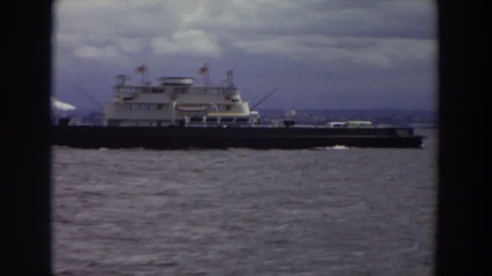 1964 Washington 8mm frame showing a large ferry with white decks and dark hull moving across cloudy water.