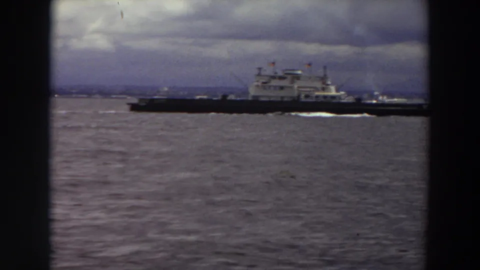 Final 8mm frame of the ferry continuing rightward across cloudy Washington waters with shoreline in the distance.