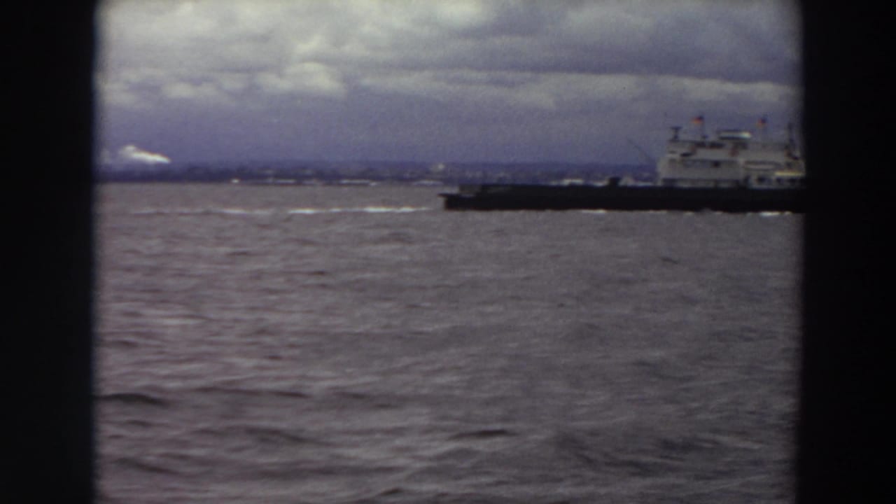 Large ship crossing choppy water under an overcast sky with dark vertical borders.