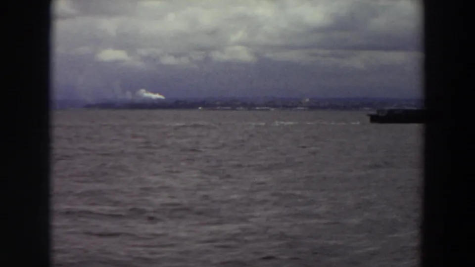 1964 Washington coastal view with gray water, low distant shore, cloudy sky, and a partial vessel edge at the right frame.