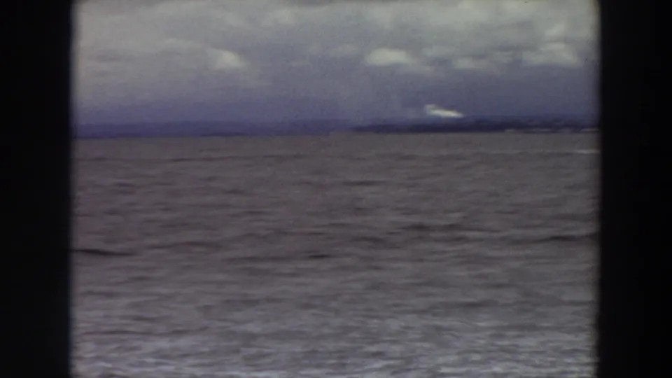 1964 Washington home-movie view of broad coastal water with a dim shoreline and overcast sky, framed by dark borders.