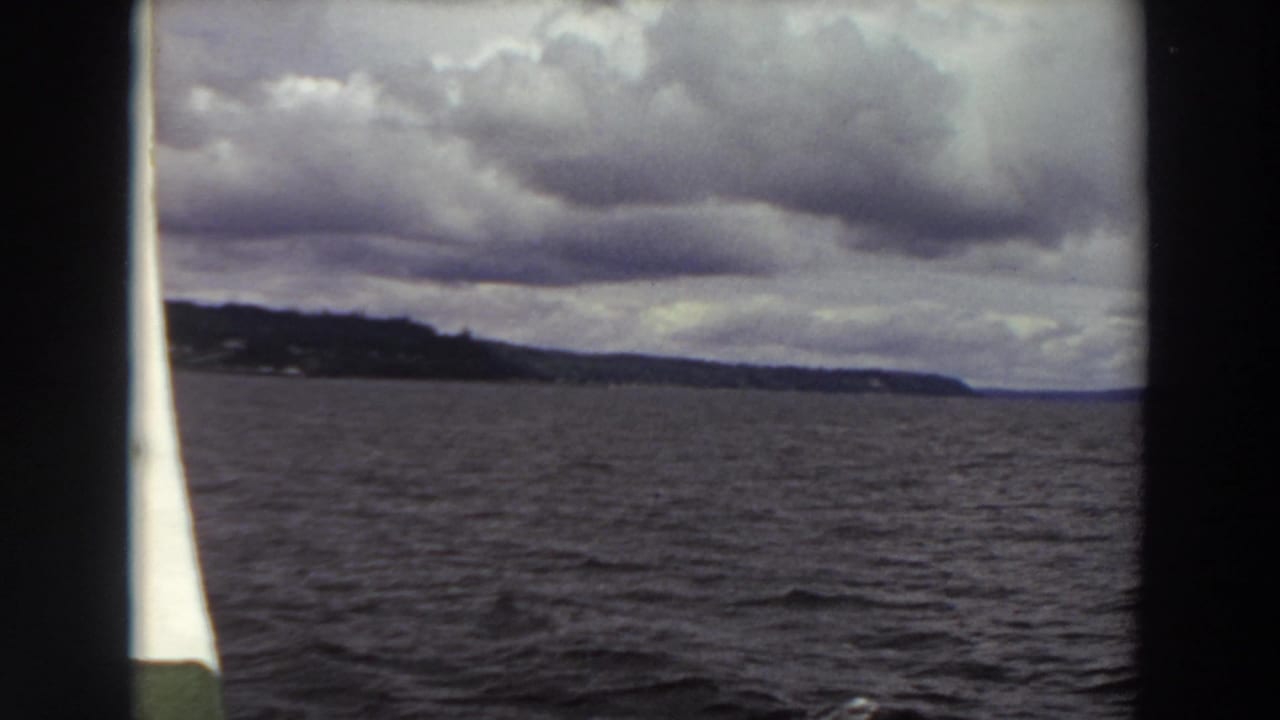 Cloudy water view with distant shoreline framed by dark boat structure.