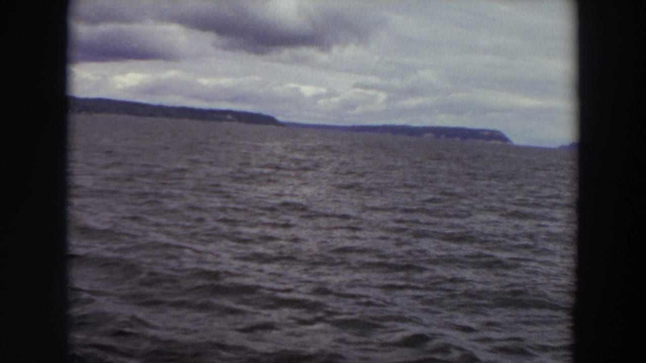 1964 Washington 8mm frame showing choppy water and a low distant coastline under layered clouds.