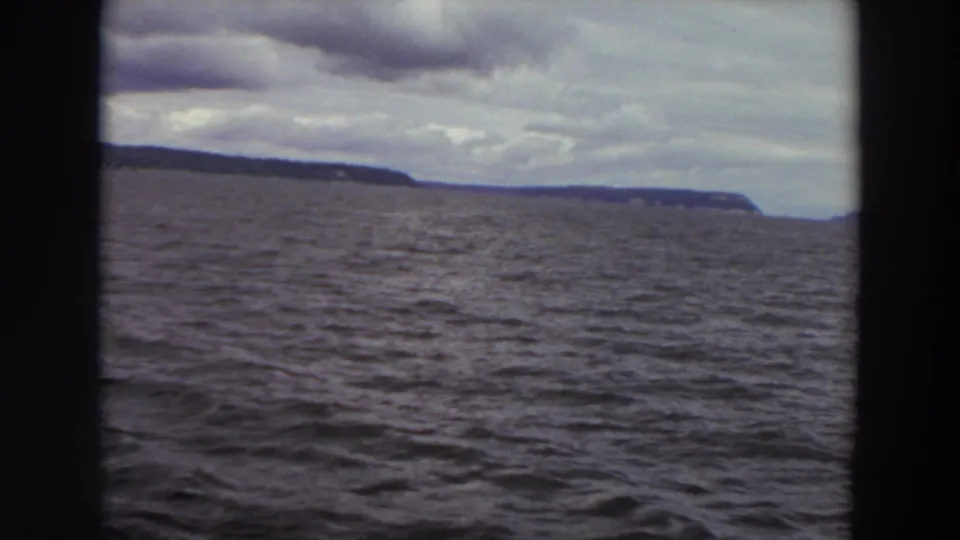 1964 Washington 8mm frame showing choppy water and a low distant coastline under layered clouds.