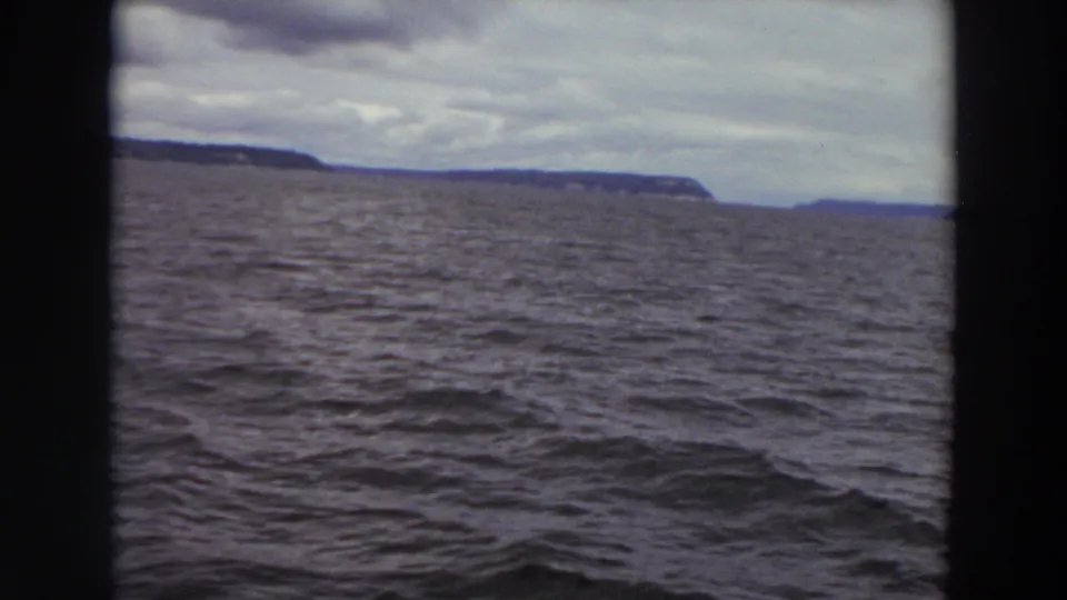 A Washington coastal view from the water, with waves in front and a low dark shoreline under overcast clouds.