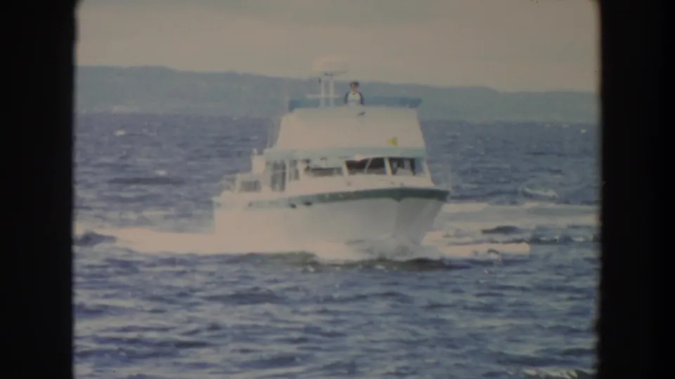The cruiser fills more of the frame as it rides over choppy water, leaving a broad white wake beneath an overcast sky.