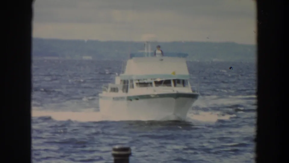 White motor yacht approaches across choppy Washington water, with a small figure visible on the upper deck.