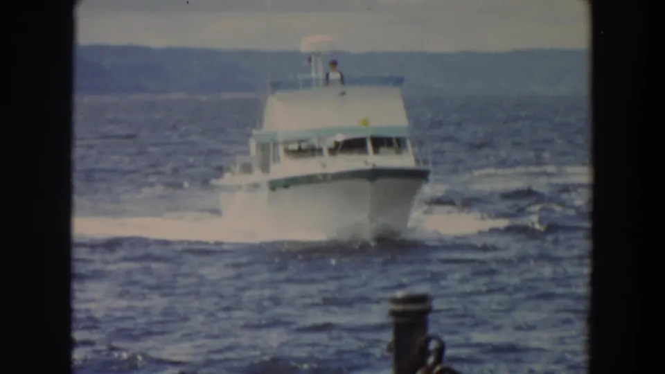 Close home-movie view of a white motor yacht with a visible person on the upper deck and spray along the hull.
