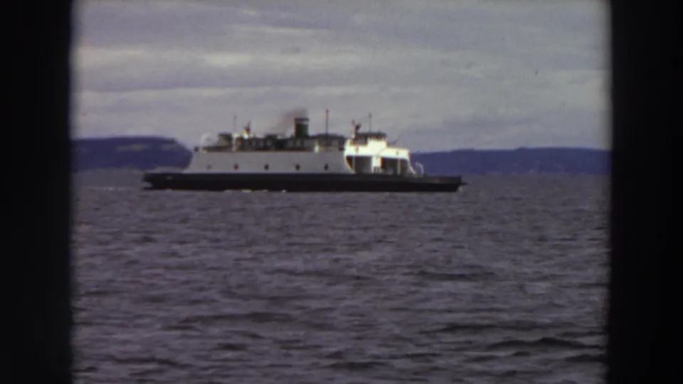 Vintage 8mm view of a ferry in profile on Washington waters, framed by dark film edges and a cloudy horizon.