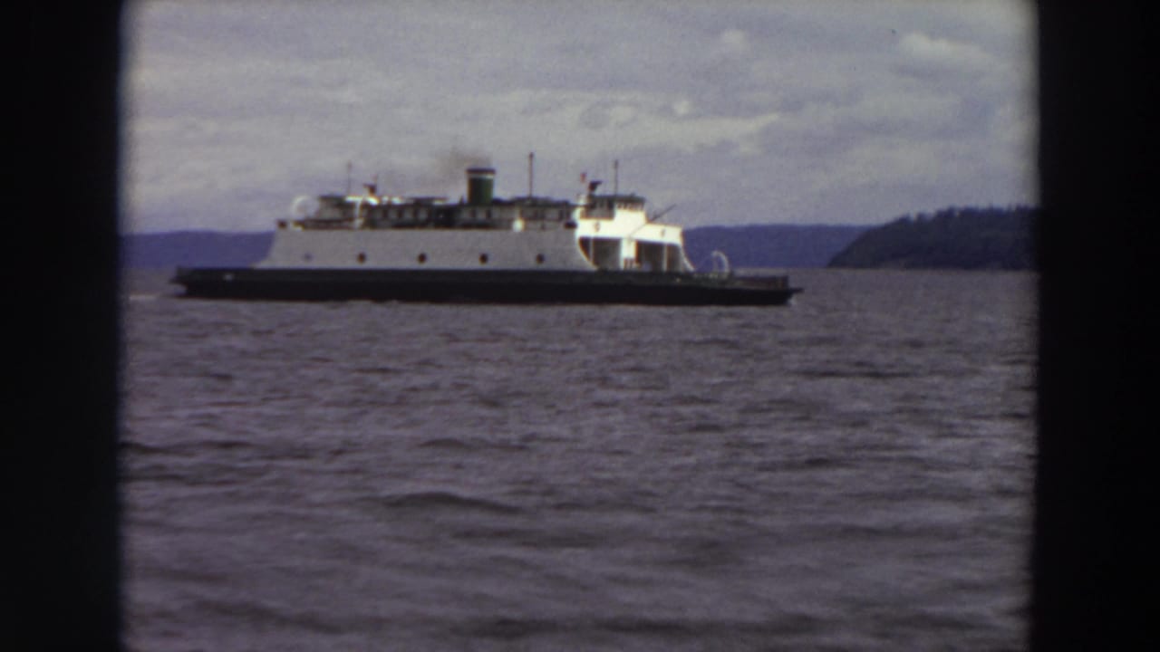 Ferry travels across a waterway with hills and shoreline in the distance.