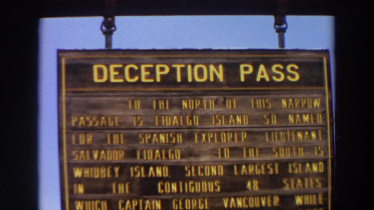 1964 Washington 8mm frame showing the upper portion of a hanging Deception Pass history sign against a clear blue sky.