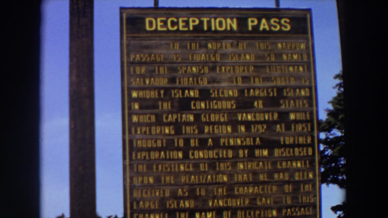 Close view of a Deception Pass historical sign with yellow lettering against blue sky.