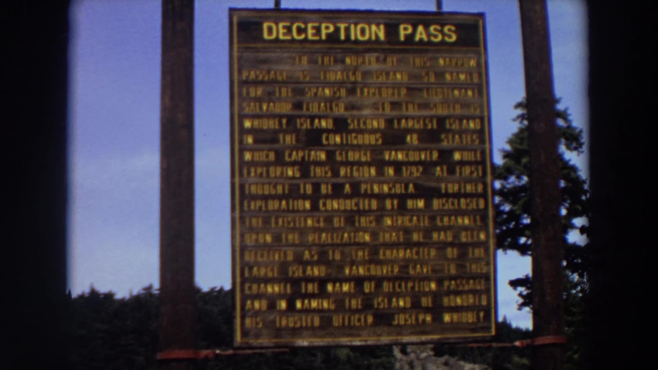 Deception Pass historical marker framed by wooden posts and trees.
