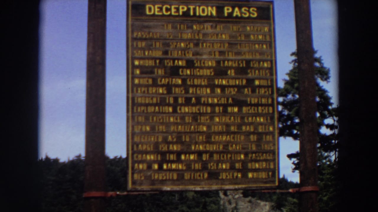 1964 Washington home-movie frame of the Deception Pass historical marker, partially softened by 8mm focus and film grain.
