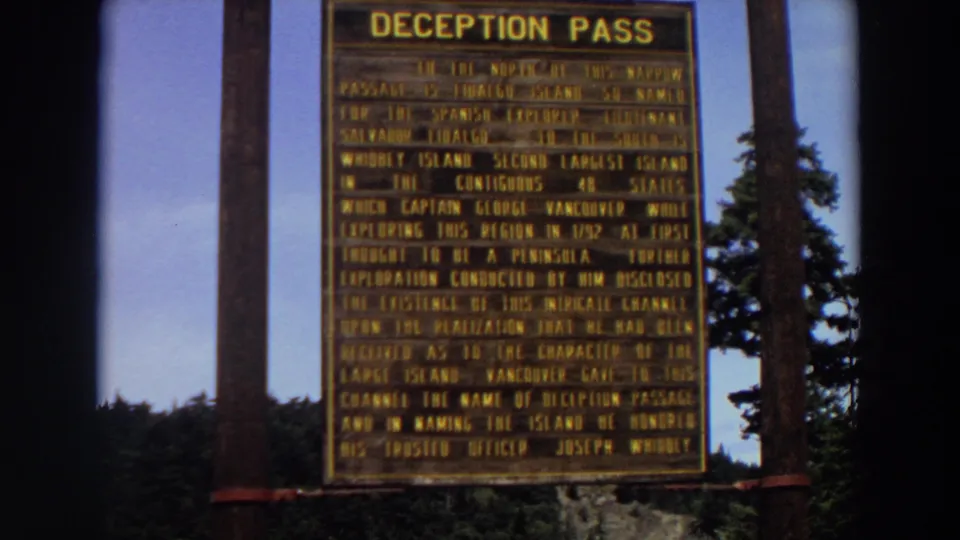 1964 Washington home-movie frame of the Deception Pass historical marker, partially softened by 8mm focus and film grain.