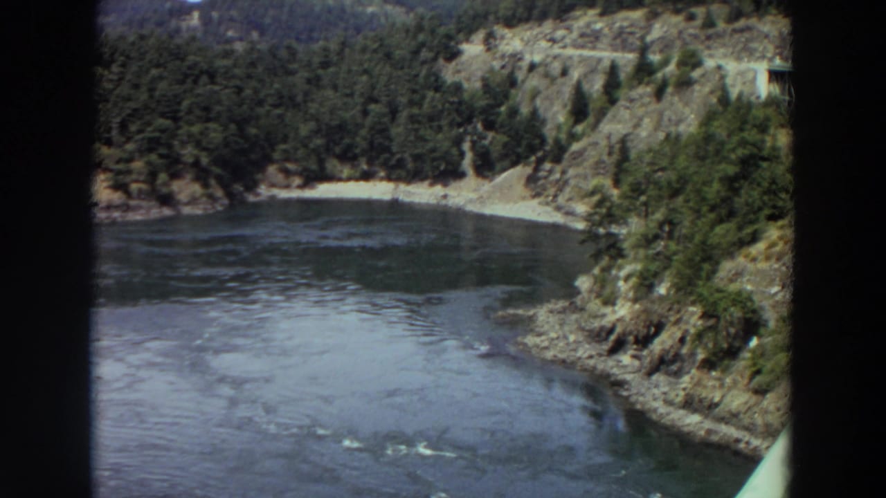 River bend below forested hills with rocky shoreline and dark water.