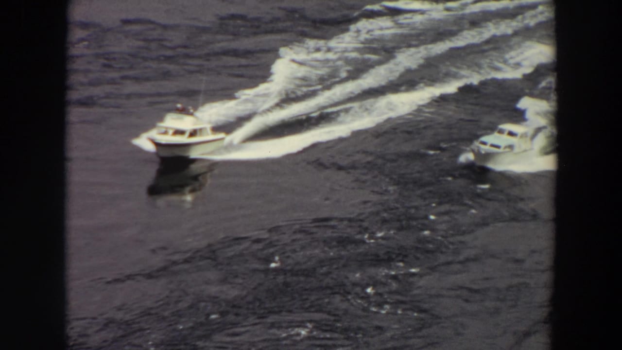 1964 Washington 8mm frame of two white motorboats speeding across dark water with long foamy wakes.