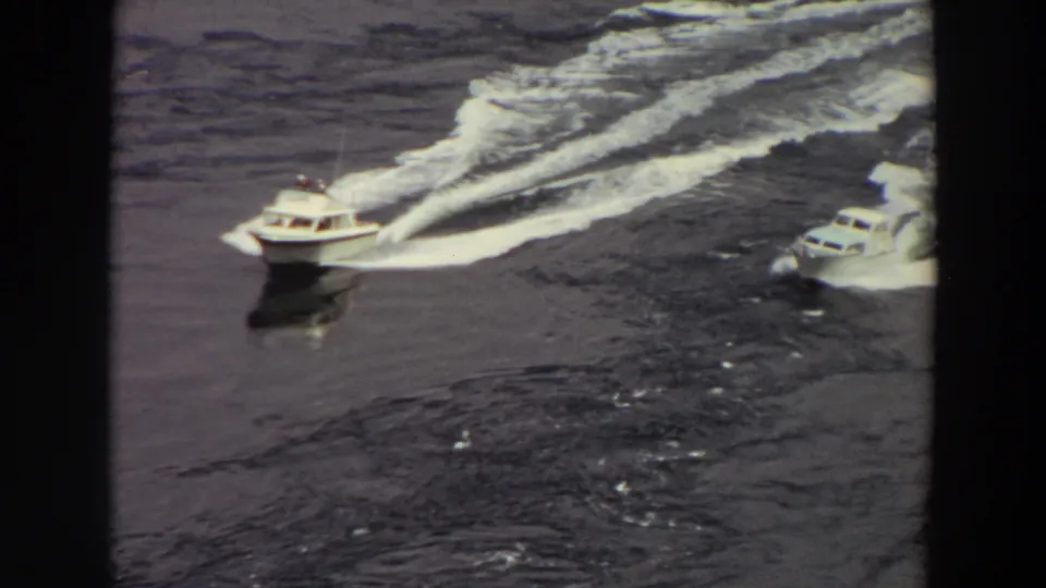 1964 Washington 8mm frame of two white motorboats speeding across dark water with long foamy wakes.