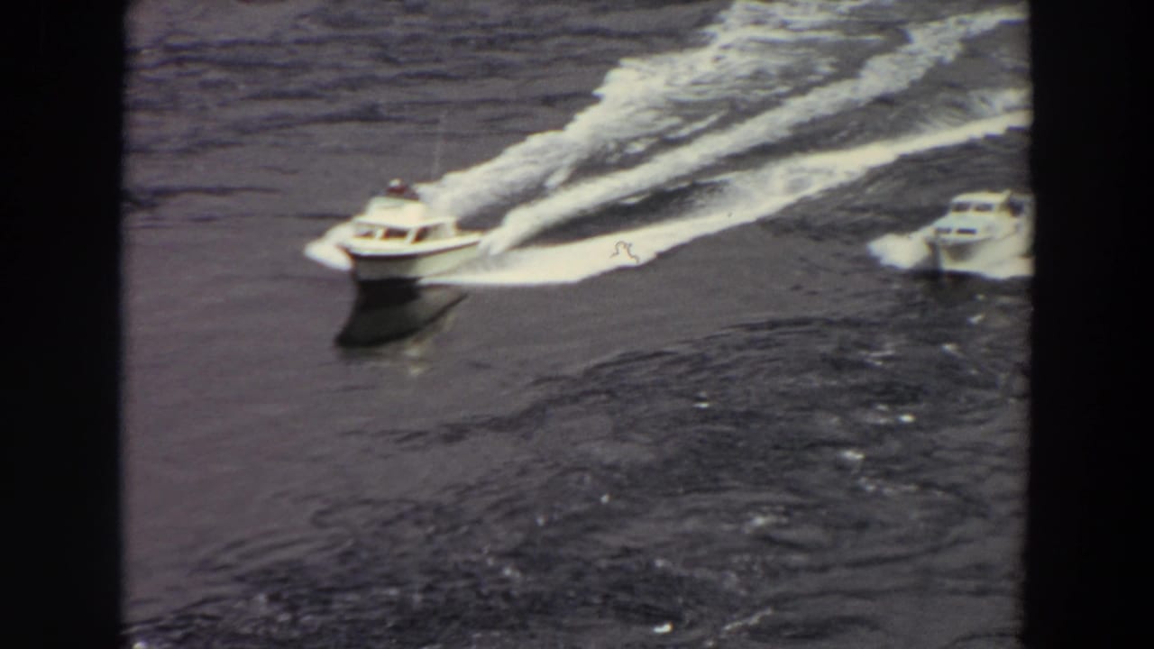 Washington home-movie frame showing motorboats on open water, one leading with a broad white wake behind it.