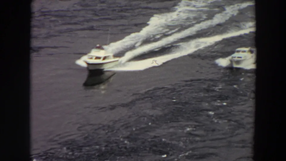 Washington home-movie frame showing motorboats on open water, one leading with a broad white wake behind it.
