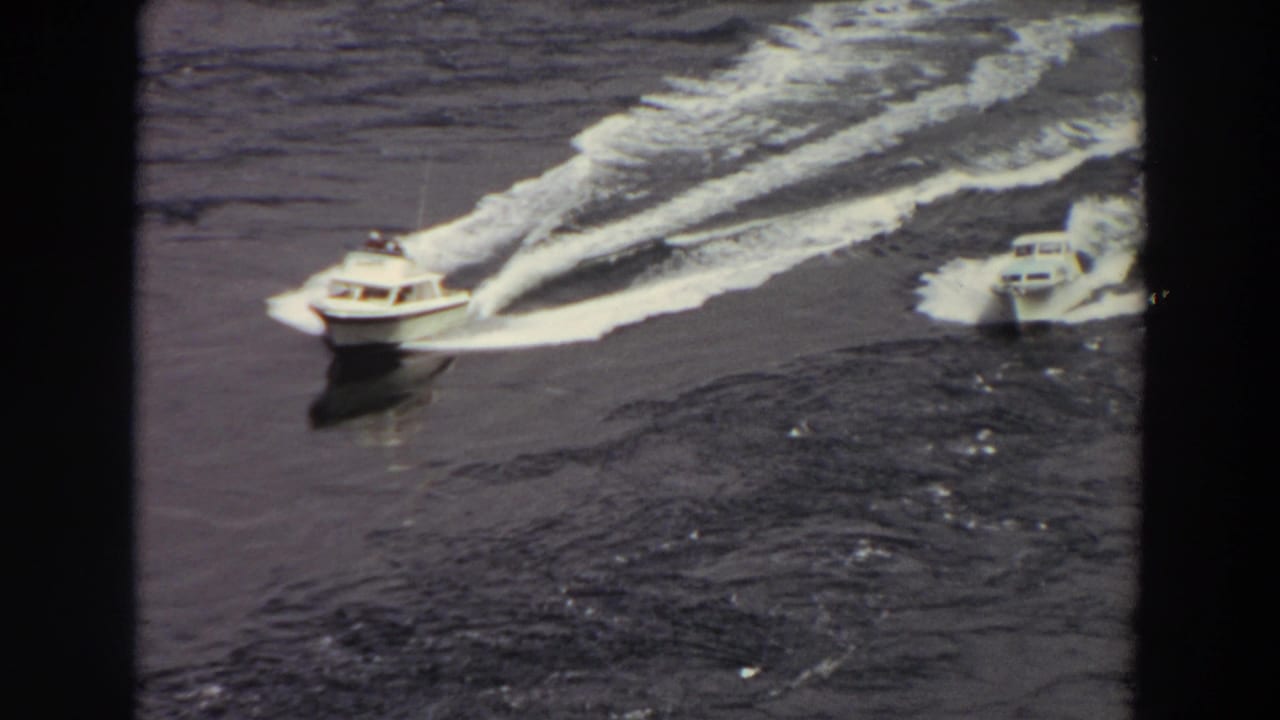 Two white speedboats cross dark water, leaving long foamy wakes.