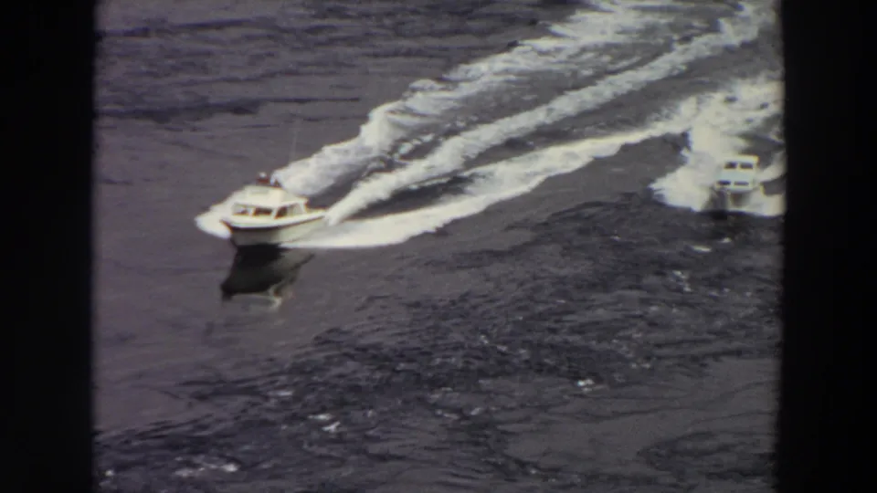 1964 Washington home-movie frame with two speedboats crossing the water, their wakes forming bright arcs behind them.