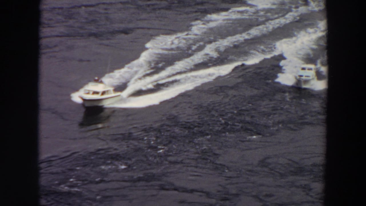 1964 Washington 8mm frame showing two small motorboats on dark water, with foamy wakes spreading behind them.