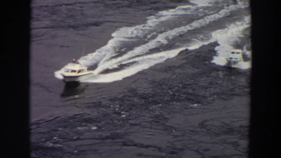 1964 Washington 8mm frame showing two small motorboats on dark water, with foamy wakes spreading behind them.