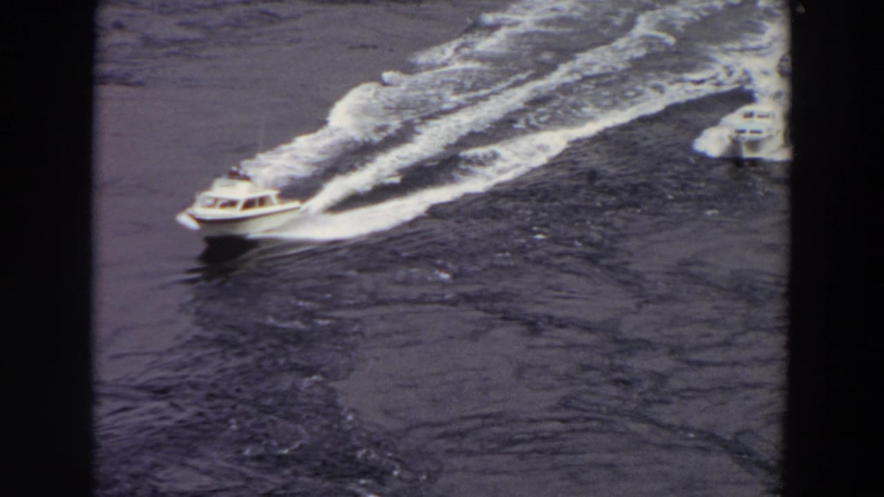 1964 Washington 8mm frame showing two small motorboats moving across calm dark water from a high-angle viewpoint.