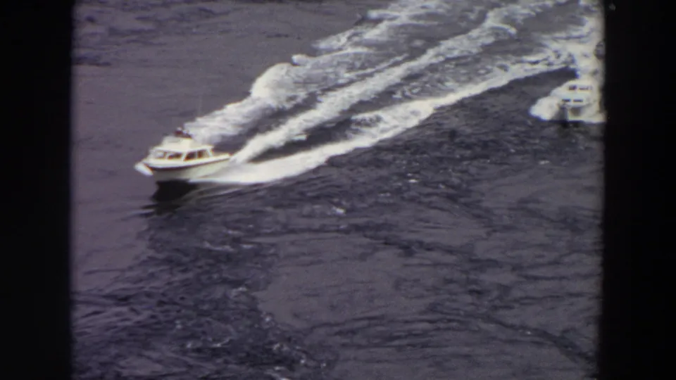 1964 Washington 8mm frame showing two small motorboats moving across calm dark water from a high-angle viewpoint.