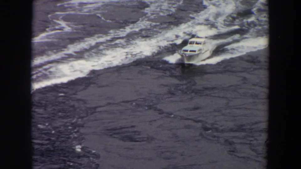A white motorboat speeds through choppy Washington water in 1964 home-movie footage, leaving a pale wake behind it.