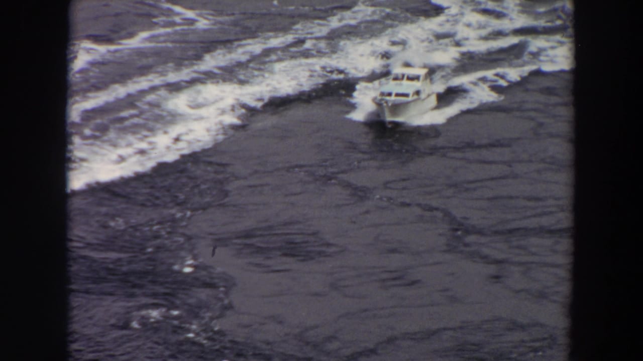 The boat continues across rough water, seen from above with foaming wave lines and no visible passengers or shoreline.