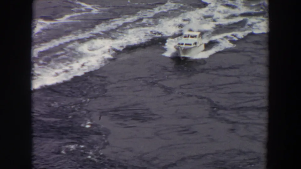 The boat continues across rough water, seen from above with foaming wave lines and no visible passengers or shoreline.