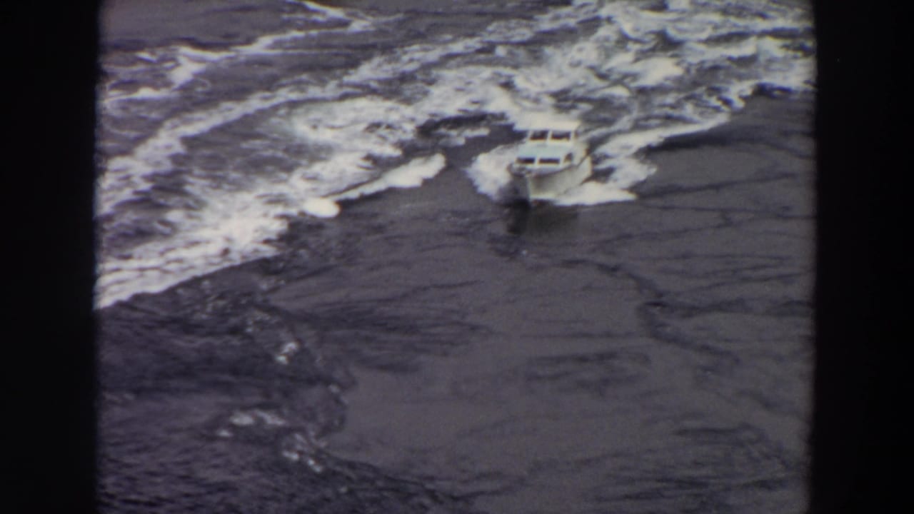 A small white motorboat travels across the frame, surrounded by broken foam and dark rippled water in 8mm footage.