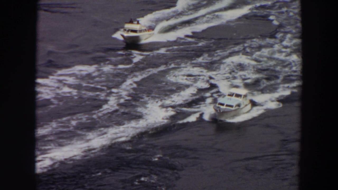 Two motorboats appear on rough Washington water, one nearer the top and another lower in frame, both surrounded by foamy wake.