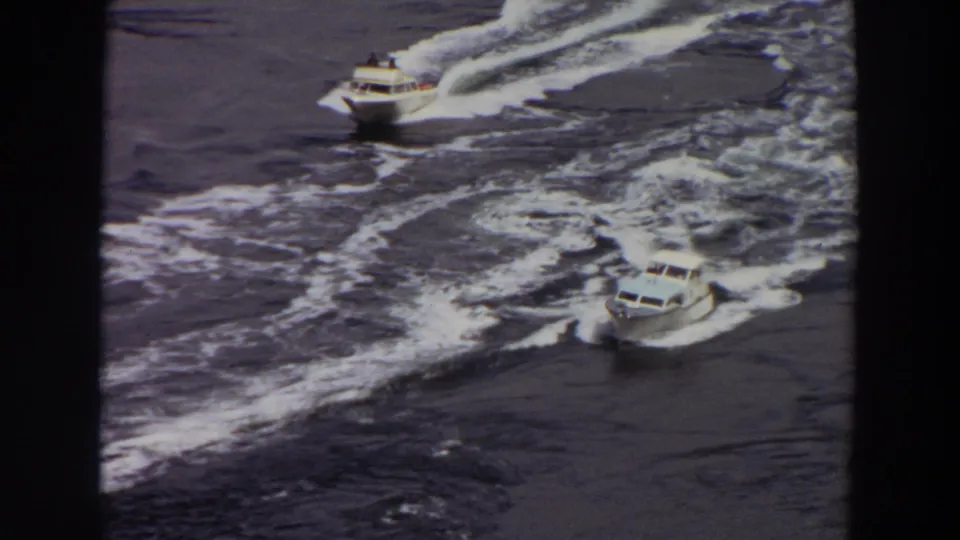 Two motorboats appear on rough Washington water, one nearer the top and another lower in frame, both surrounded by foamy wake.