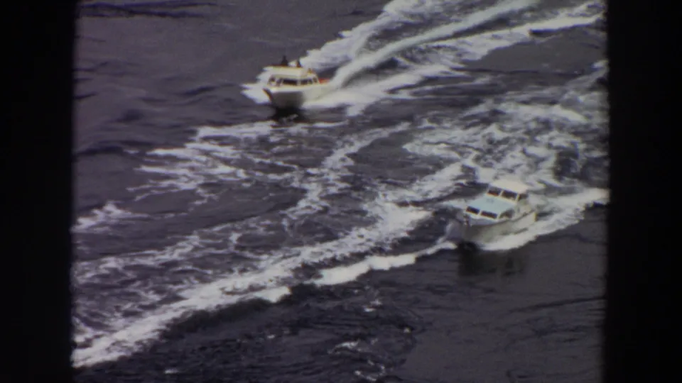 1964 Washington 8mm frame showing two small white motorboats moving across open water from an elevated viewpoint.