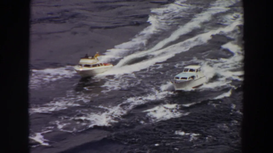Final frame of two small white motorboats crossing open water, with passengers faintly visible and wakes behind them.