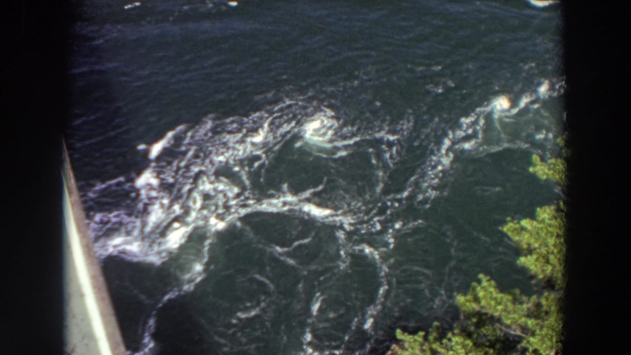 1964 Washington home-movie frame showing rough river current, frothy whitecaps, eddies, and green foliage near the riverbank.