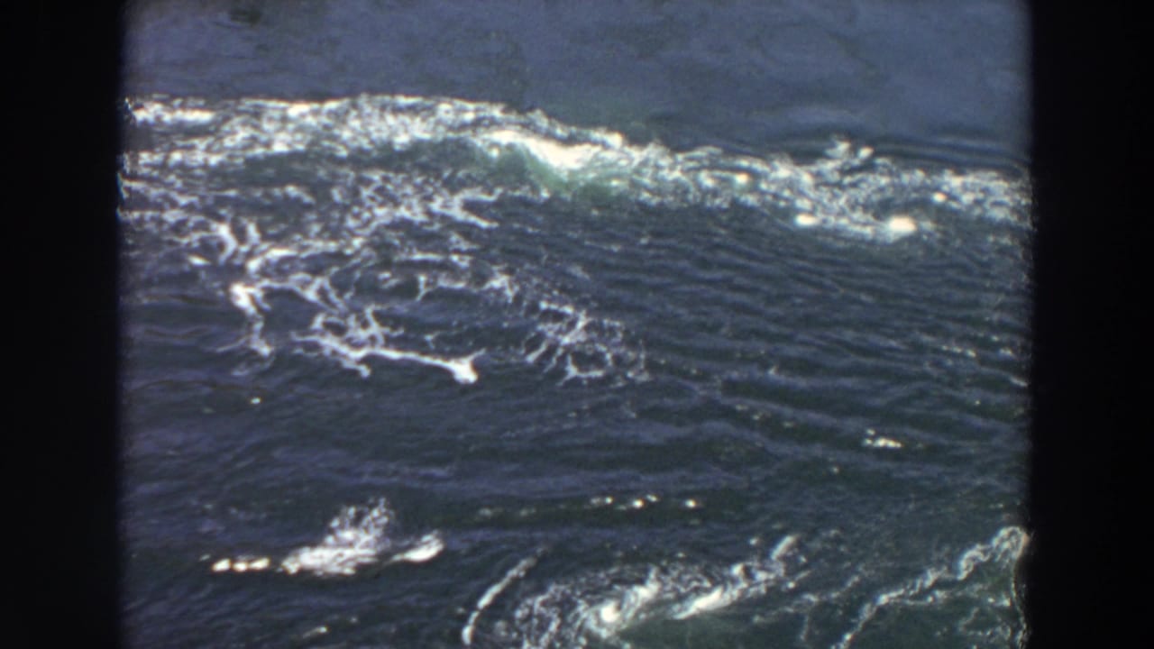 1964 Washington 8mm view of a wide, dark river surface with bright foam bands and visible turbulence across the water.