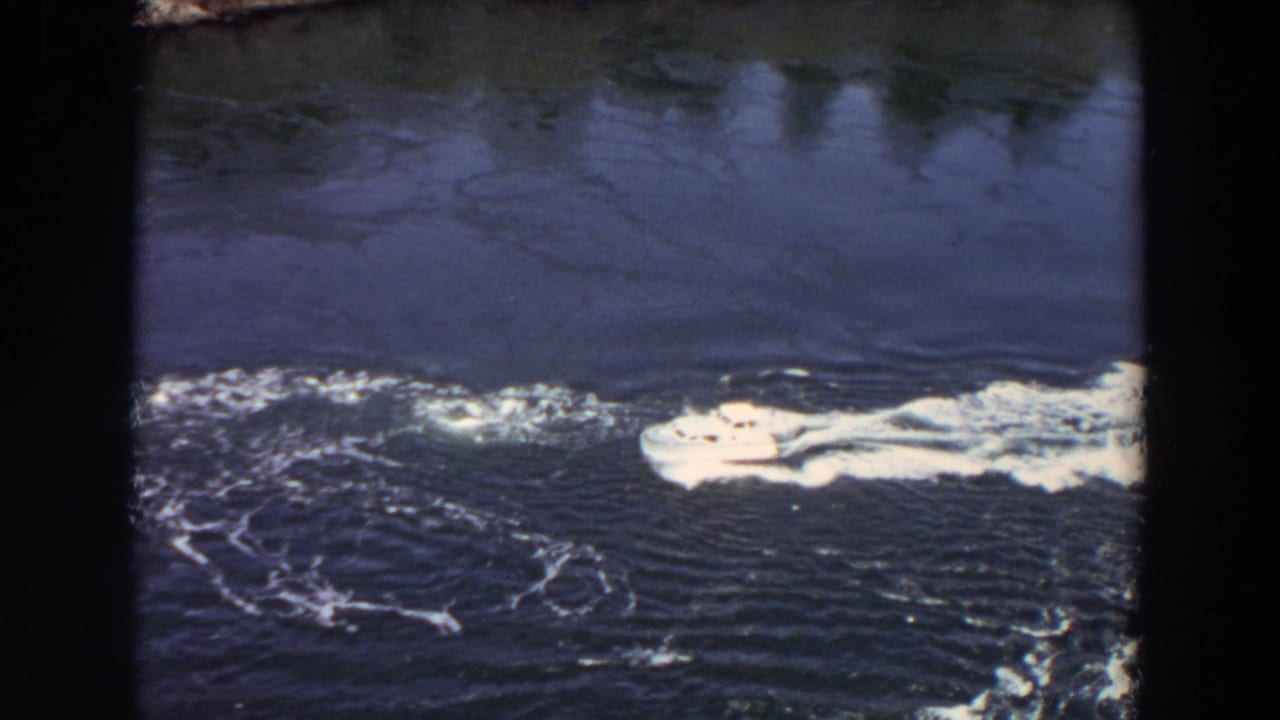 The yacht continues through the Washington inlet, its wake cutting across dark rippled water in a 1964 8mm frame.