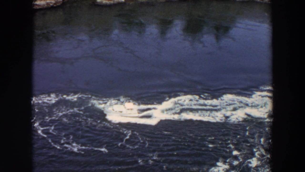 A closer 8mm view shows the white yacht moving through dark Washington inlet water with froth widening around the hull.