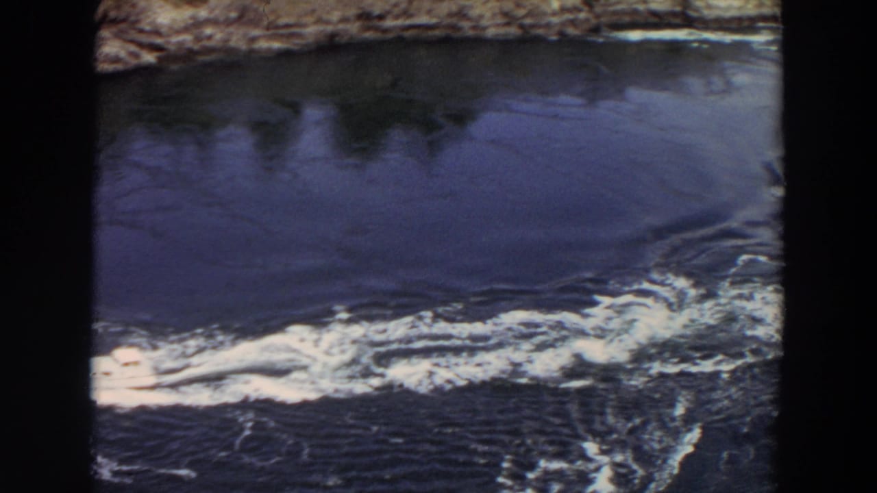 The yacht moves partly toward the frame edge as its frothy wake dominates the dark inlet water in this 1964 Washington home movie.