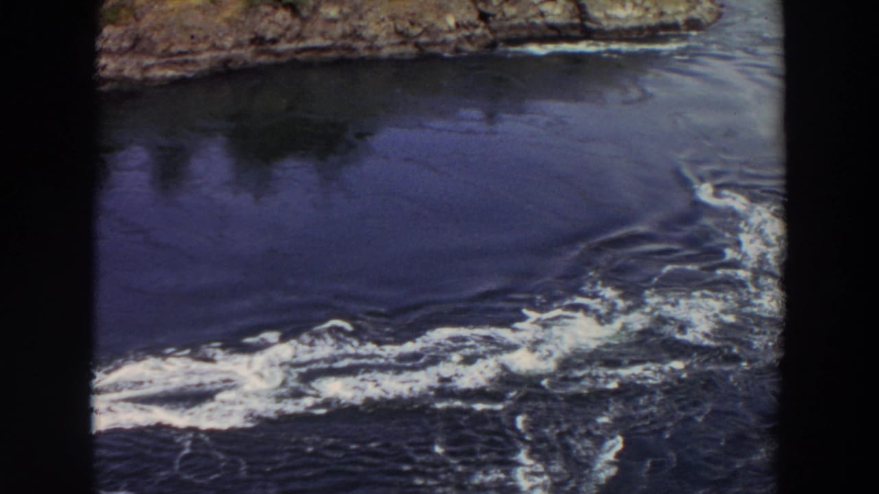 Turbulent whitewater flows from a rocky outlet into darker lake water.